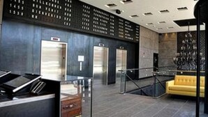A modern lobby with a reception desk, elevators, and a yellow sofa. - Z Hotel New York (Long Island City)
