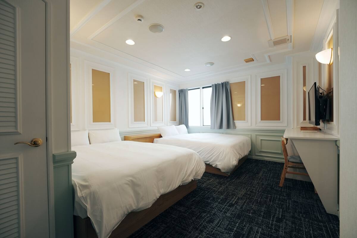 Een hotelkamer met twee bedden, een bureau, een stoel en een raam met gordijnen.