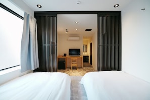 A hotel room with two beds, a desk with a chair, a television, and an air conditioning unit. - Lumi Hotel Tokyo Shinkoiwa (Tokyo)