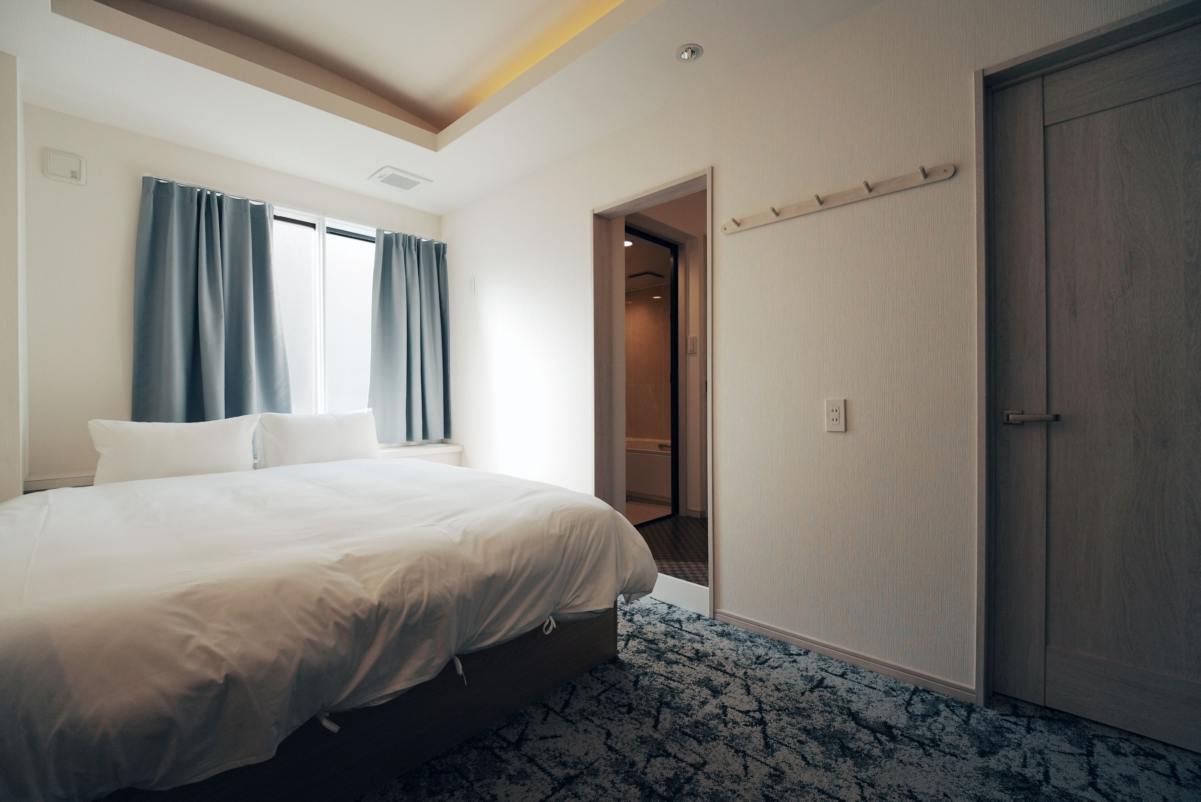 Una habitación de hotel con cama, puerta y ventana con cortinas.