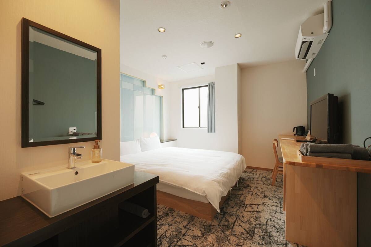 Een moderne hotelkamer met een groot bed, nachtkastje, televisie, bureau en badkamer met wastafel en spiegel.