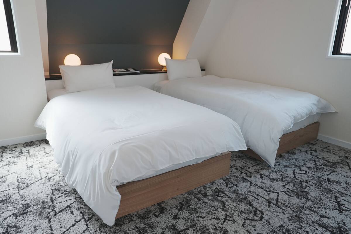 Een slaapkamer met twee bedden, een kamerbreed tapijt en een wandlamp.
