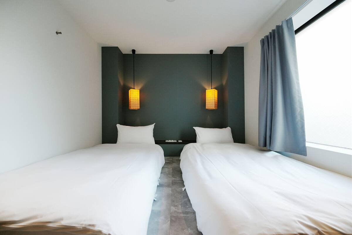 Een hotelkamer met twee bedden, een donkere muur en een raam met gordijnen.