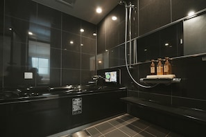 Un baño moderno con pared de azulejos negros, un lavamanos con pantalla digital, un cabezal de ducha de mano y un estante con artículos de aseo.
