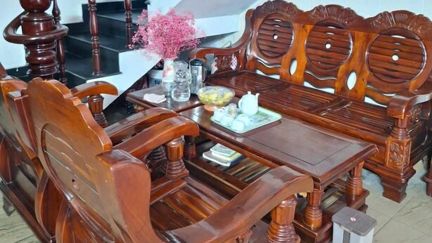 A dining area with a wooden table and chairs, a vase with pink flowers, and a staircase in the background. - Hoang Long Hotel SG by BAY LUXURY (Ho Chi Minh City)