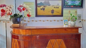 A reception desk with a wooden finish and diamond-patterned panels, a framed painting of a landscape, and a television mounted on the wall. - Hoang Long Hotel SG by BAY LUXURY (Ho Chi Minh City)