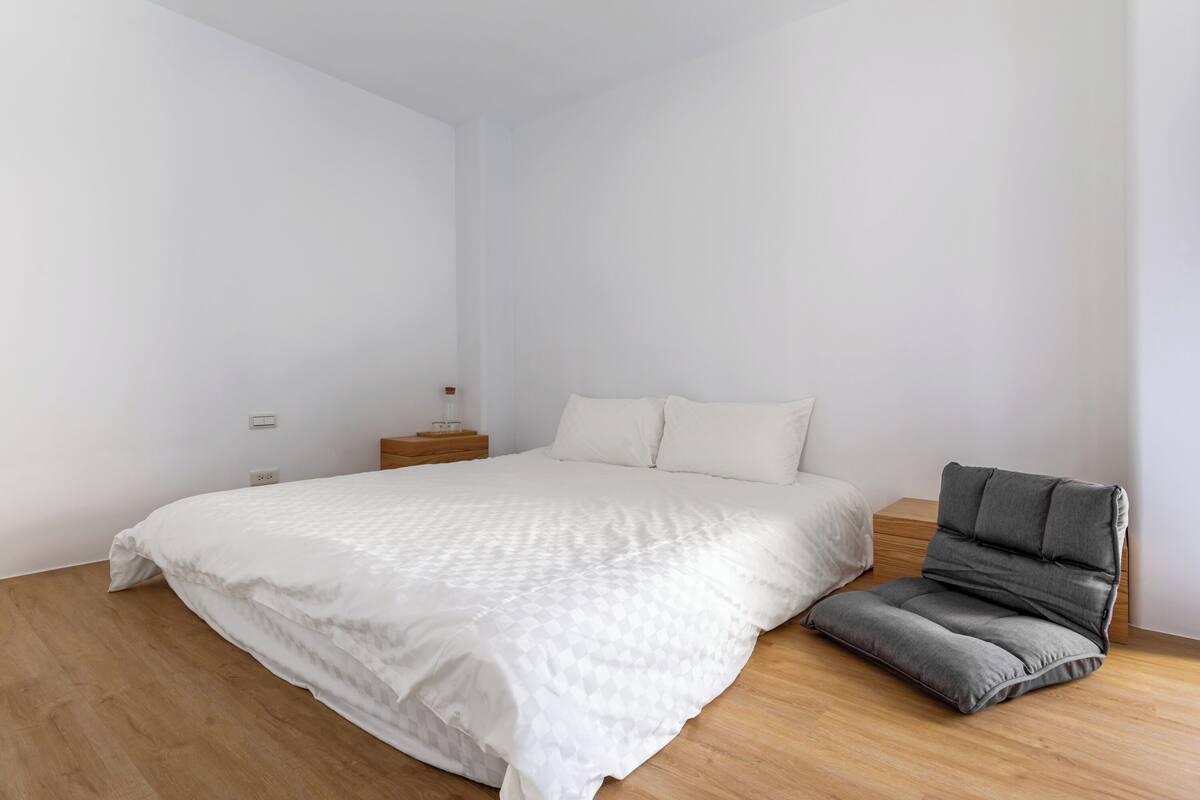 A minimalist bedroom with a bed, bedside table, and a chair.