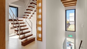 A modern staircase with wooden steps and metal railings, a wooden accent wall with illuminated letters, and a view of the outside through a window. - Unknown Coffee Inn (Liuqiu)