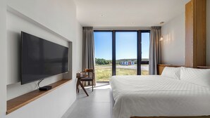 A modern hotel room with a large bed, a flat-screen TV mounted on the wall, a wooden bedside table, and a large window offering a view of the outdoors. - Unknown Coffee Inn (Liuqiu)