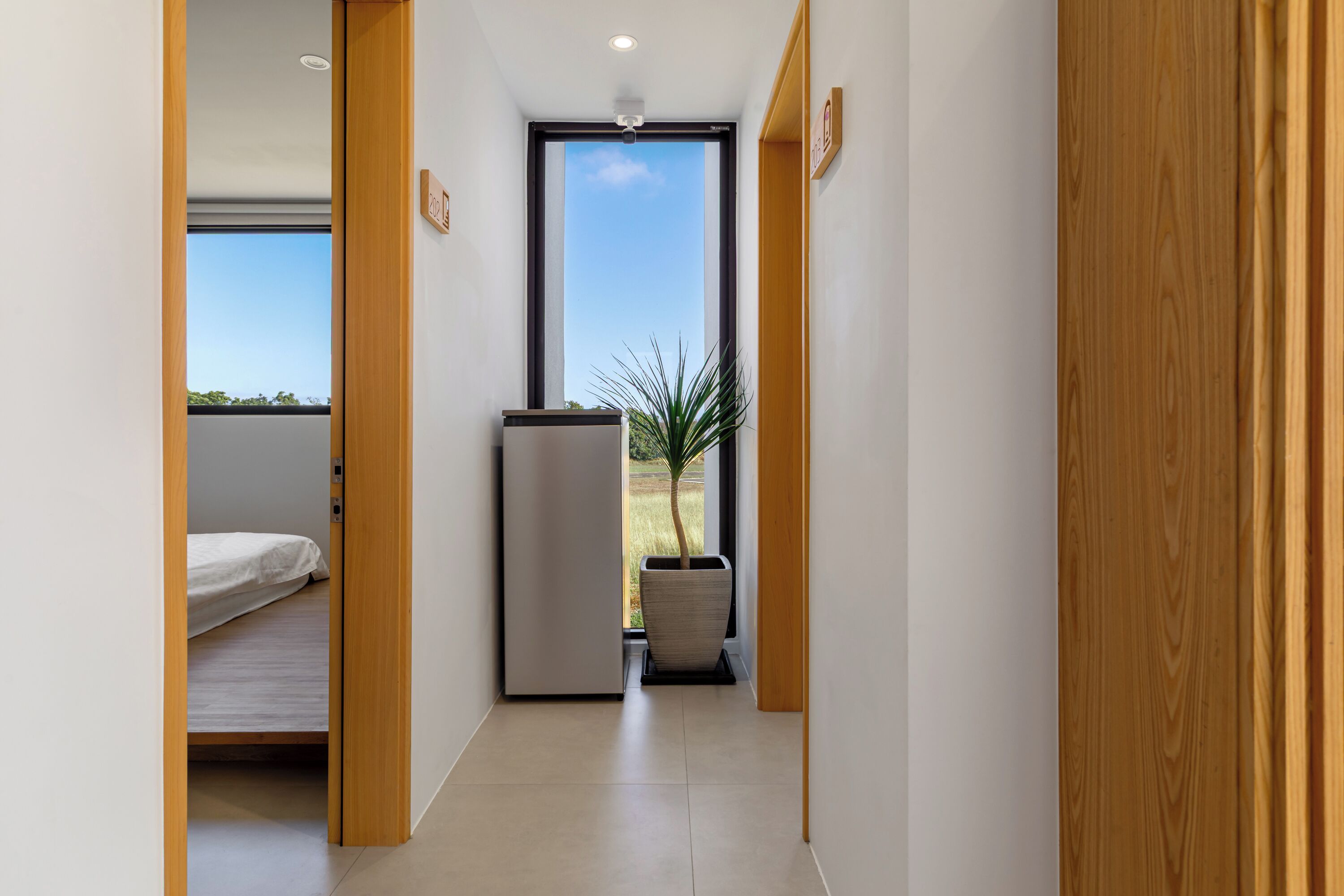 Un pasillo estrecho con una cama, un refrigerador y una planta en maceta.