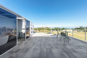 A modern outdoor terrace with a clear view of the landscape, a glass-enclosed area with a seating arrangement, and a large window offering expansive views.