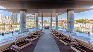Una piscina infinita con tumbonas de madera, vistas despejadas de la ciudad y un diseño arquitectónico moderno.