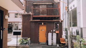 A building with a wooden door, two large white tanks, and a chair outside. - Ivy Place Harajuku Urban Steel Teahouse (Tokyo)