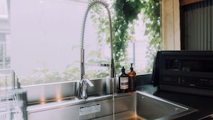A kitchen with a stainless steel sink, a faucet, and a microwave. There are two bottles on the counter, one labeled "ORGANIC" and the other "YAMAHA." - Ivy Place Harajuku Urban Steel Teahouse (Tokyo)