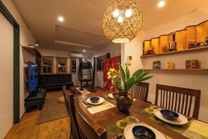 A dining area with a wooden table, chairs, a vase with flowers, and a hanging light fixture. - GARDEN HOUSE (Osaka)