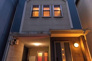 Un edificio con fachada plana, una puerta con panel de vidrio y un pequeño letrero iluminado encima.