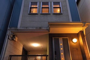 Un bâtiment à la façade plane, avec une entrée bien visible marquée par une porte et un balcon doté de balustrades.