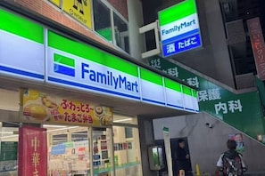 A FamilyMart store with a green and white sign, a visible entrance, and a person standing outside. - GARDEN HOUSE (Osaka)