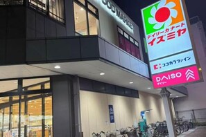 A building with a large sign for a supermarket and a bicycle parking area. - GARDEN HOUSE (Osaka)