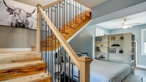 Une chambre avec un escalier en bois, un lit, une table de chevet, une bibliothèque et un ventilateur de plafond.