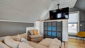 Un salon moderne avec un canapé d’angle, un canapé plus petit et un fauteuil jaune. On y trouve une cheminée surmontée d’un écran noir.