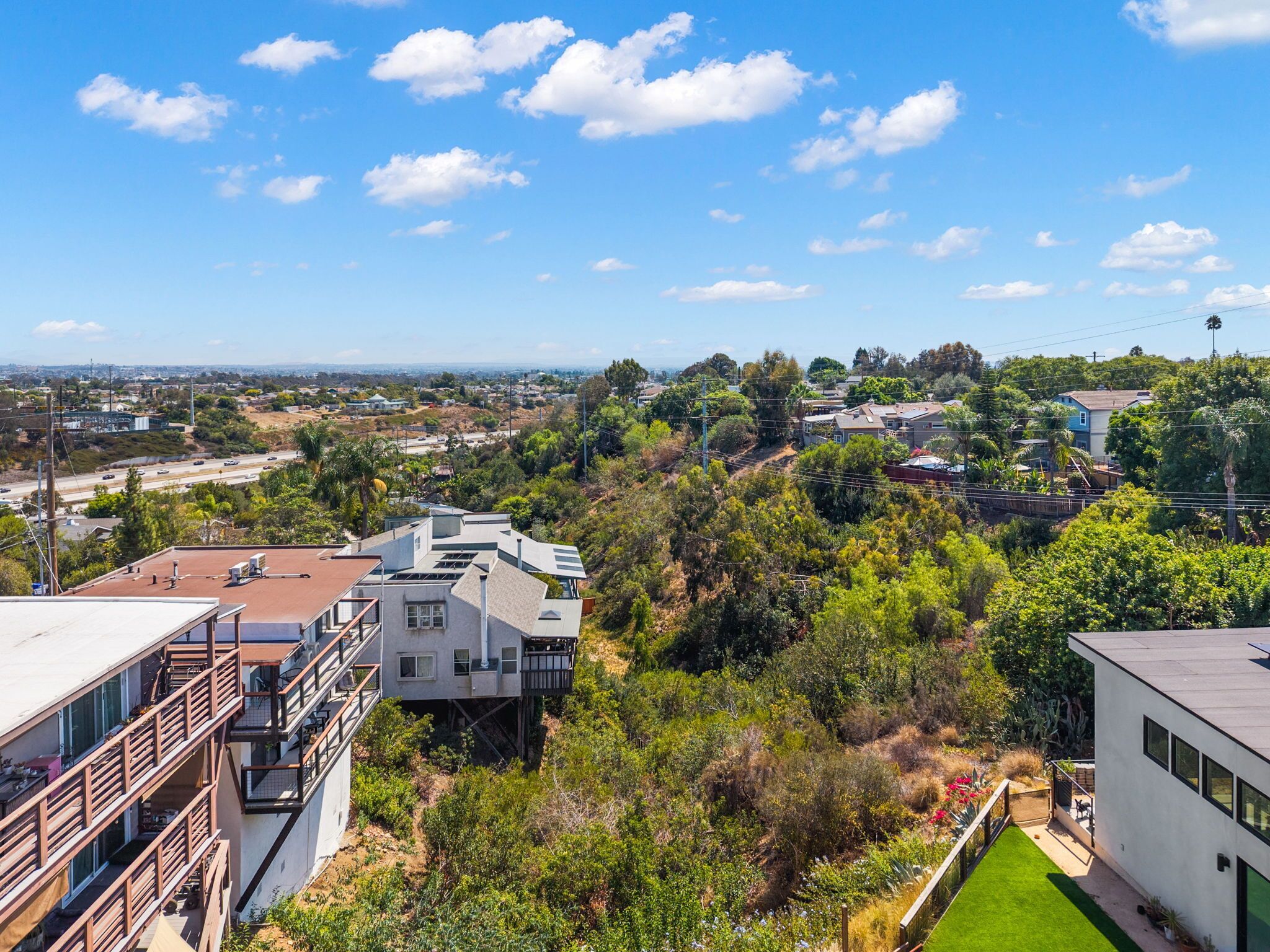 Un barrio residencial con casas modernas, cielo despejado y una autopista a lo lejos.