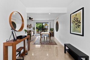 Un interior moderno con una consola de madera, un área de comedor con sillas, un banco y una obra de arte grande enmarcada en la pared.