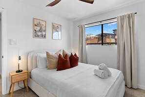 Un dormitorio moderno con una cama grande, una mesita de noche con lámpara y una ventana con cortinas.