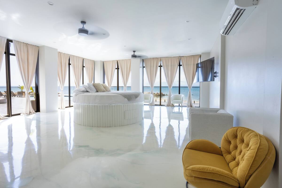 Une chambre moderne et spacieuse, dotée d’un grand lit rond blanc et d’un fauteuil jaune.
