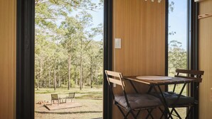 Una habitación con una mesa y sillas de madera, vista a un bosque a través de un ventanal grande, y un termostato en la pared.
