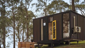 A small wooden cabin with a single door, a window, and an air conditioning unit. - Three-Kalm by Tiny Away (Rainbow Flat)