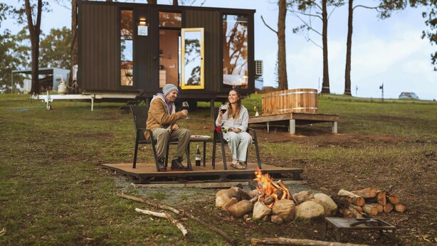 Un espacio de estar al aire libre rústico con una fogata, una terraza de madera y una cabaña al fondo.