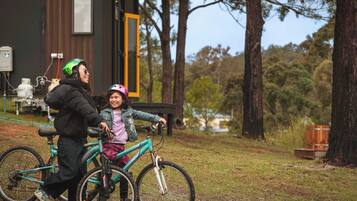 Una persona en bicicleta con un niño, un edificio con una puerta y árboles al fondo.