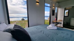 Ein Schlafzimmer mit einem großen Bett, Blick auf die Landschaft und einer kleinen Sitzecke mit Tisch und Stühlen.