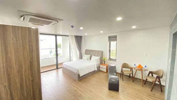 A modern hotel room with a large bed, a desk with chairs, and a view of the outdoors. - Golden Hotel SG by BAY LUXURY (Ho Chi Minh City)
