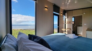 A bedroom with a large window offering a view of a lake and distant landscape. - Aorangi Peak Cabins 9 by Tiny Away (Rotorua)