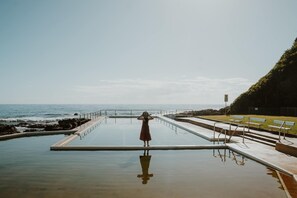 A swimming pool with a person standing at the far end, overlooking the ocean.