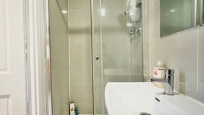 A bathroom with a glass-enclosed shower, a white sink, and a mirror. - 2BR Stylish Beacon Retreat in Tulsa (Tulsa)