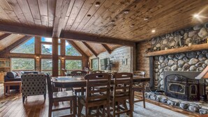 A cozy cabin interior with a stone fireplace, wooden dining table, and large windows offering a view of the surrounding forest. - Mountain cabin w/ deck & lake access (Terra Alta)
