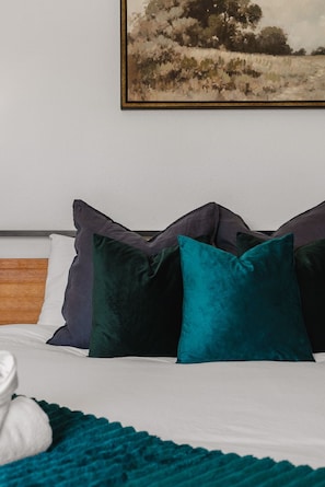 Una cama con sábana blanca, almohadas verde azulado y oscuro verdosas, y una manta verde azulado.