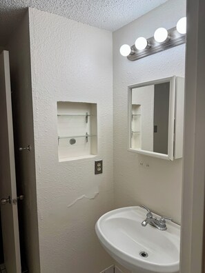 A bathroom with a white sink, a mirror, and a light fixture above the mirror.