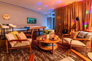 A cozy living room with a wooden coffee table, comfortable seating, a flat-screen TV, and ambient lighting. - Fall getaway: rooftop skyline views near Broadway, sleeps 12 (Nashville)