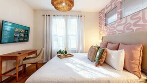 Een slaapkamer met een bed, bureau, televisie en raam met gordijnen.