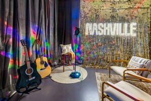 Une pièce comprenant deux guitares, un tabouret, une chaise et un panneau lumineux au néon sur lequel on peut lire « NASHVILLE ».