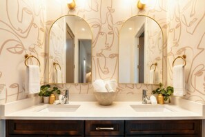 Une salle de bain avec deux lavabos, un grand miroir et un panier rempli de serviettes.