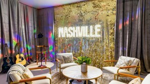 Een kamer met een ronde koffietafel, twee fauteuils, een bank en een gitaar. Een neonbord met de tekst 'NASHVILLE' hangt aan de muur.