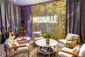 A room with a round coffee table, two armchairs, a sofa, and a guitar. A neon sign reads "NASHVILLE" on the wall. - Fall in Nashville: rooftop skyline views near Broadway, sleeps 12 (Nashville)