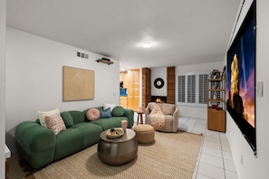 Uma sala de estar com um sofá verde, uma poltrona bege, uma mesa de centro e uma lareira.