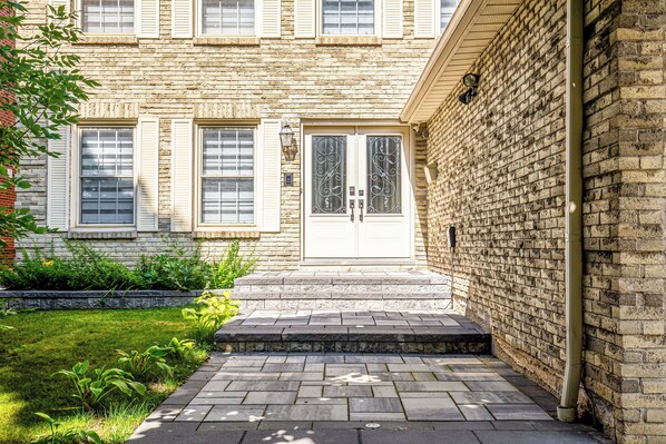 A brick building with a white door and windows, a small front garden, and a paved walkway leading to the entrance.