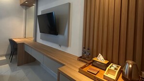 Ein modernes Hotelzimmer mit einem Holzbüro, einem flachbildfernseher an der Wand, einer kleinen Sitzecke und einer Minibar.
